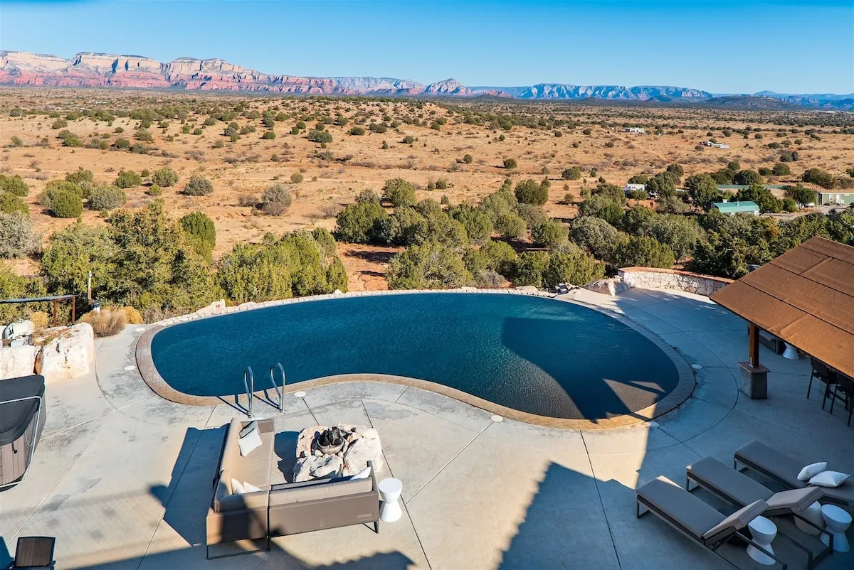 A serene exterior view featuring an infinity pool overlooking the surrounding red rock landscape, with inviting outdoor seating and a fire pit. The setting exudes tranquility and luxury, with the natural beauty of Sedona’s mountains serving as a stunning backdrop.