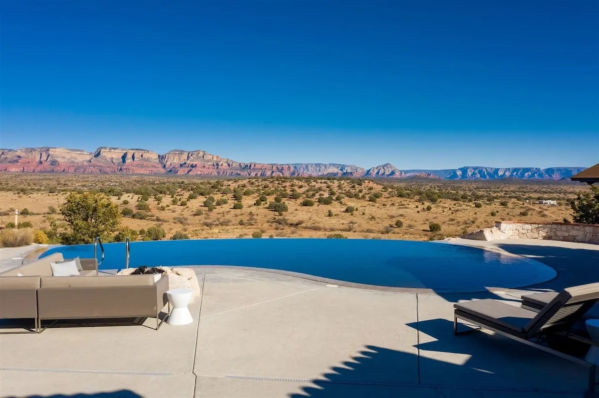 A stunning infinity pool overlooks a dramatic mountain range, with an inviting outdoor seating area nearby. The expansive vista and water feature create a tranquil ambiance perfect for relaxation and soaking in the surrounding natural beauty.