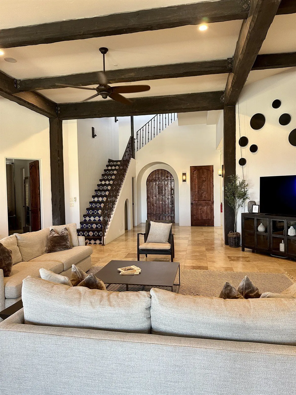 A cozy, contemporary lounge space with a sofa seating area, staircase, decorative wall, wooden doors, and a television unit. The seating is arranged for both socializing and comfortable TV viewing, ideal for movie nights and group gatherings.