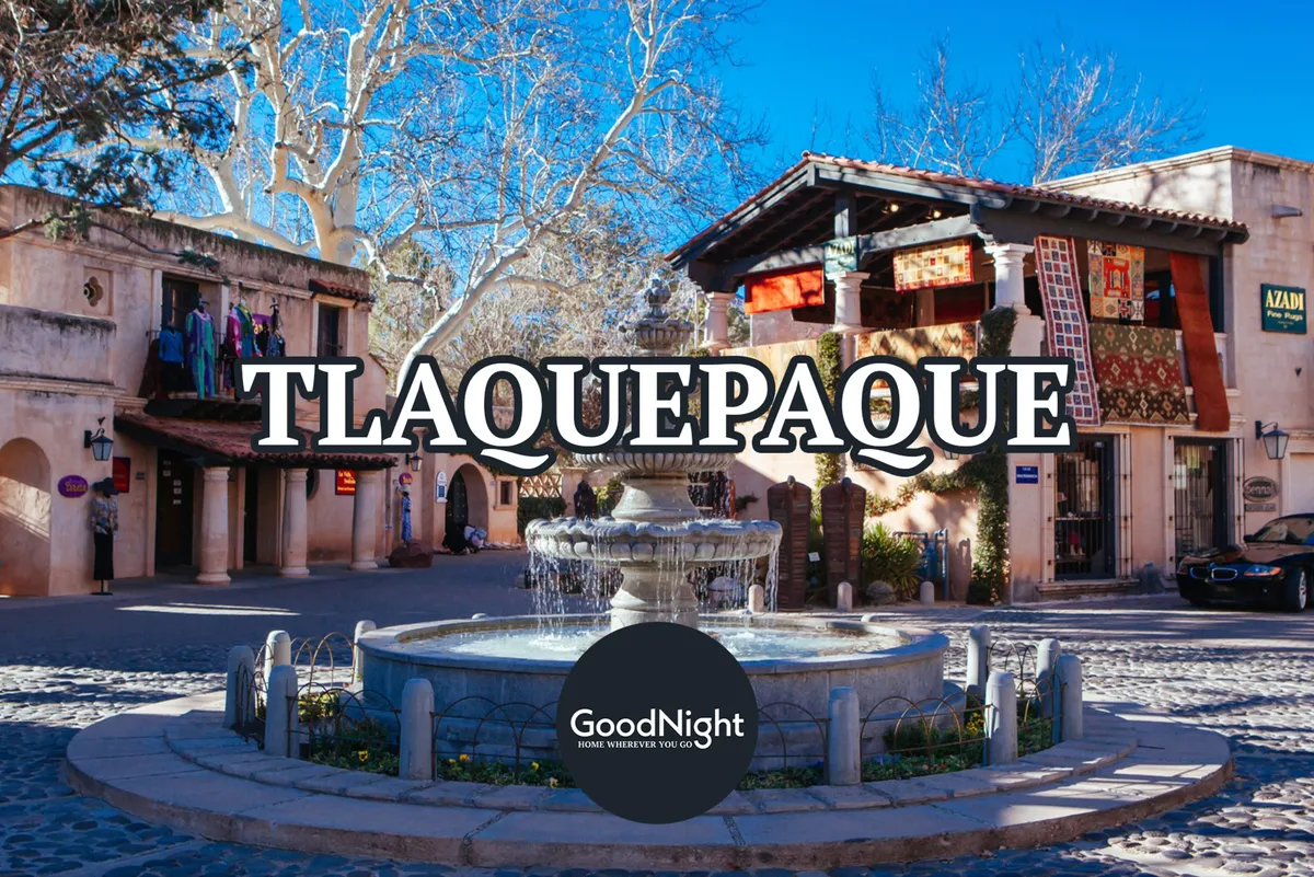 A vibrant, bustling outdoor plaza with a decorative fountain, colorful Mediterranean-style buildings, and a cobblestone pathway. The area is alive with people strolling, shopping, and exploring art, suggesting a lively cultural atmosphere and opportunities for discovery.
