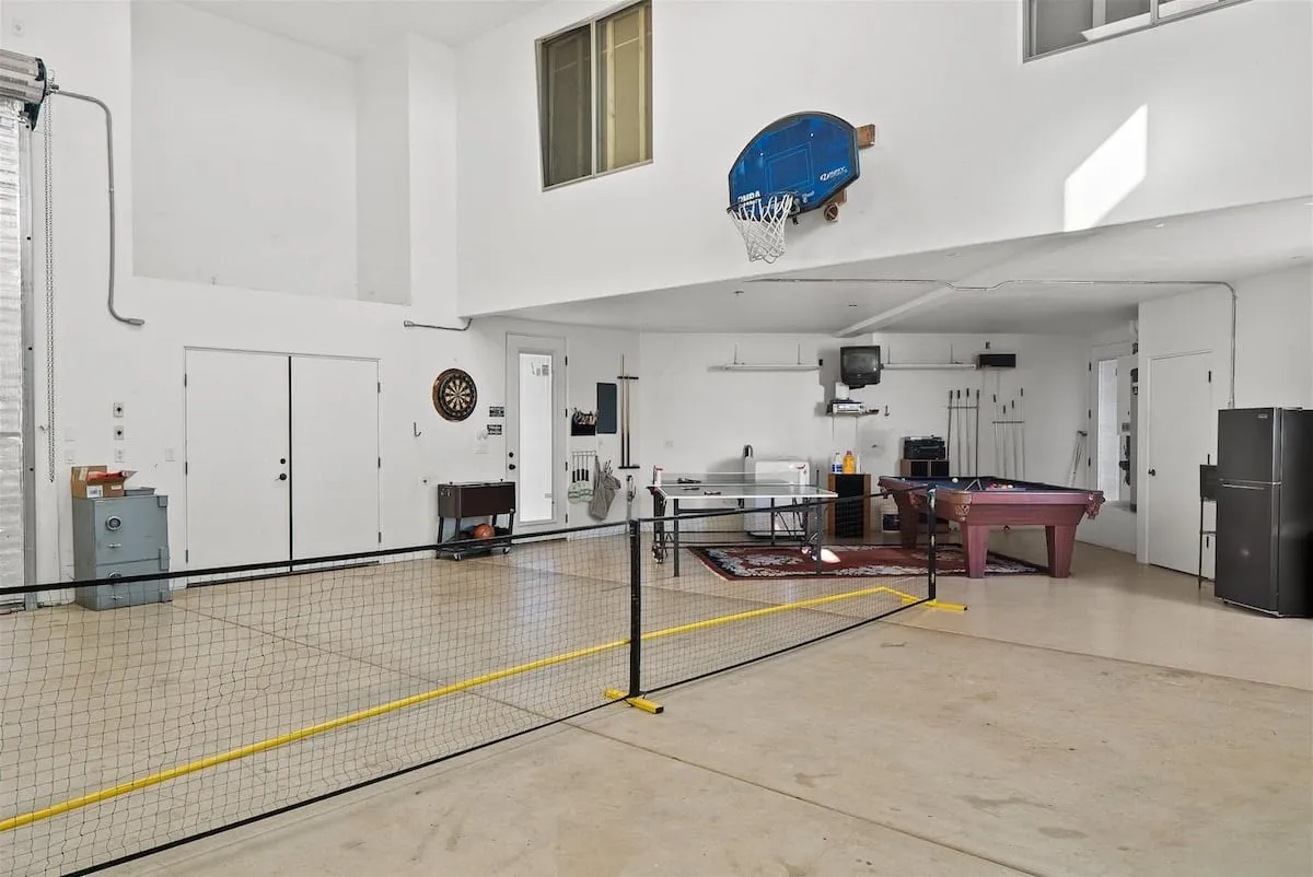 A vibrant, well-lit game room featuring a basketball hoop, ping pong table, pool table, and dartboard. The scene is set up for recreational activities with spacious layout and modern finishes, inviting guests to play and socialize.