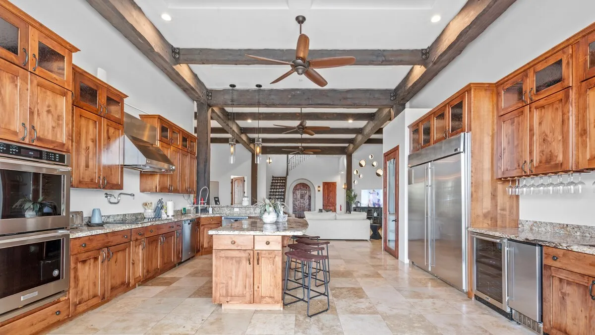 A beautifully appointed gourmet kitchen with a large island, wooden cabinets, granite countertops, and exposed wooden beams. Ample space invites both cooking and socializing, with a layout that encourages group meal preparation and casual dining.