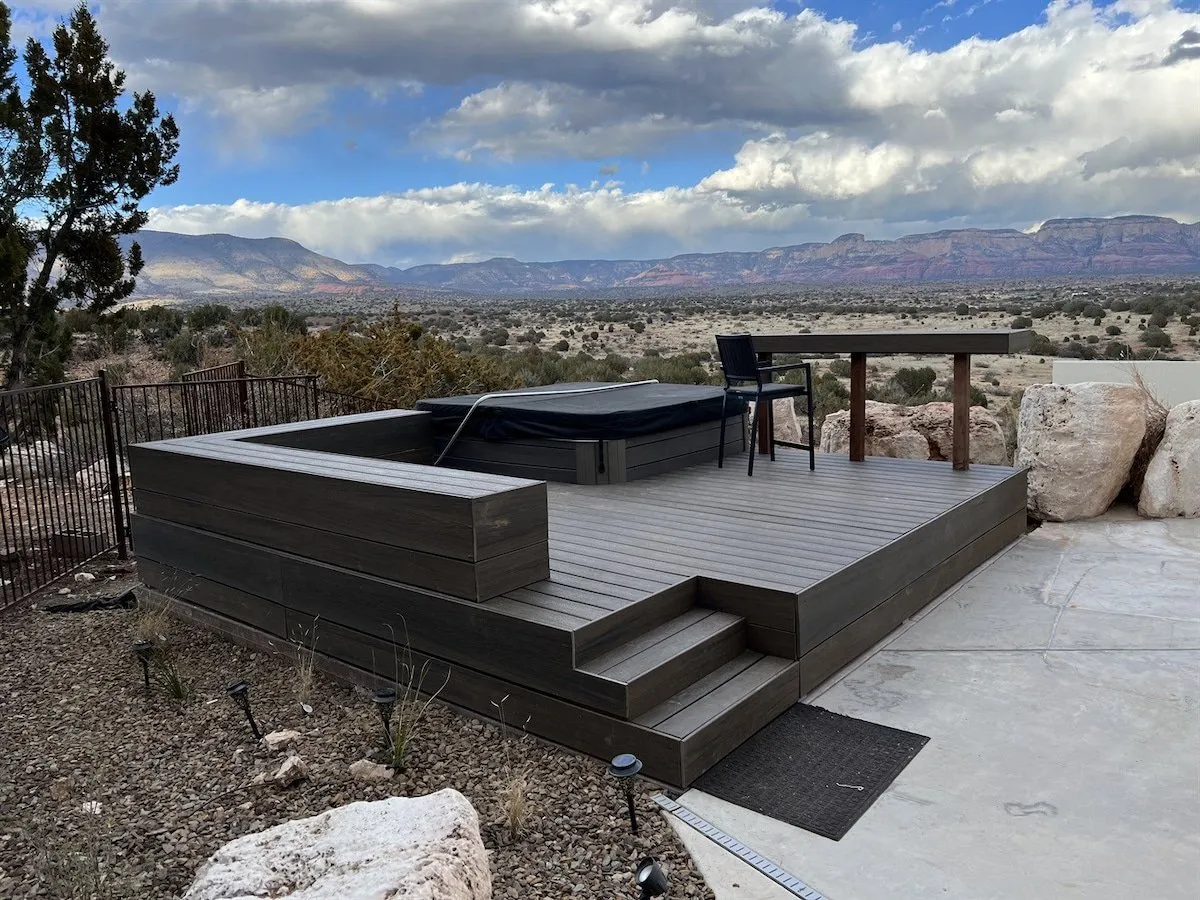 An inviting hot tub on a wooden deck overlooking mountain views, with an outdoor table and chairs nearby. The serene setting highlights opportunities for relaxation, meditation, and group gatherings in a restorative environment.