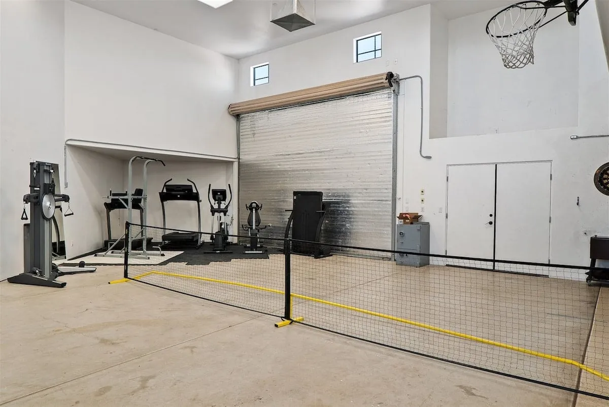 A spacious fitness area equipped with a range of exercise machines, a basketball hoop, and a netted space for various sports or fitness activities. The area is bright, energetic, and clearly designed for workouts and active play.